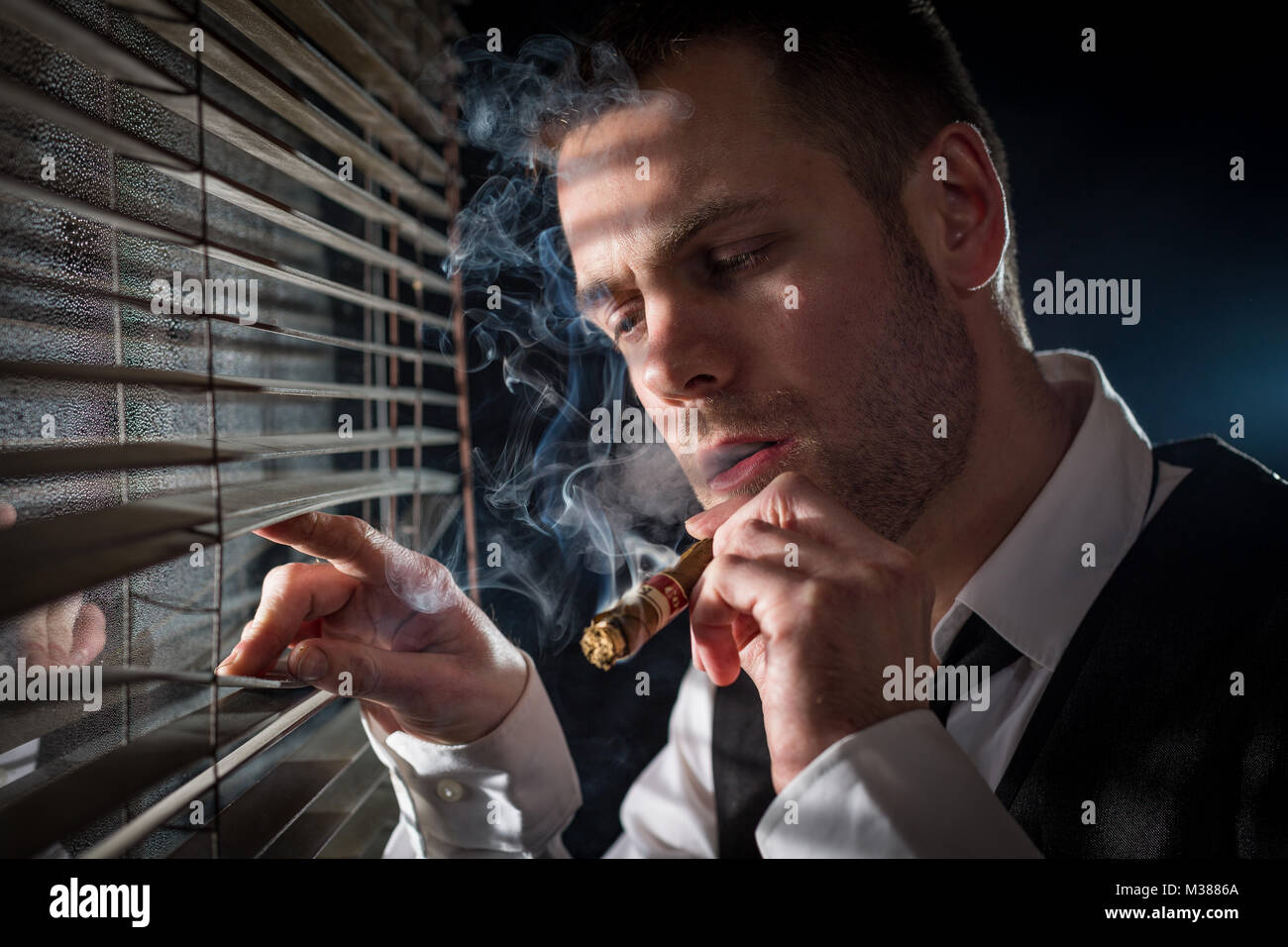 Gangster fumant un cigare tout en regardant par la fenêtre les phares d'une voiture Banque D'Images