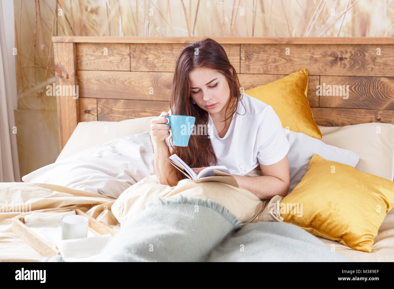 Jolie fille sur une chaise confortable avec plateau ,la lecture d'un livre, la notion de confort et de hipster. Banque D'Images