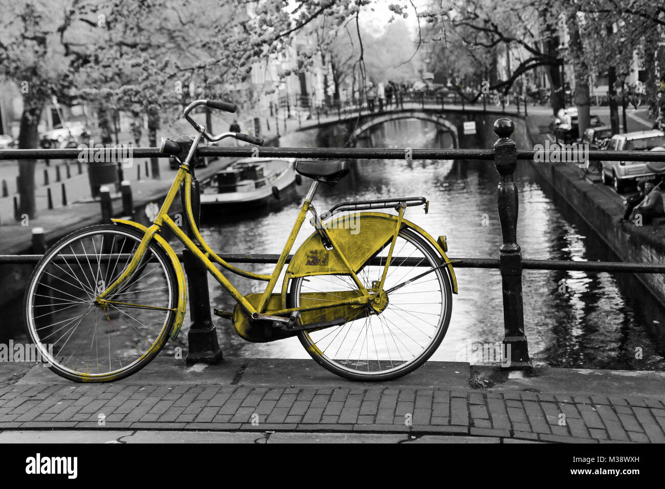 Photo d'un vélo jaune solitaire sur le pont au-dessus du canal d'Amsterdam. L'arrière-plan est noir et blanc. Banque D'Images