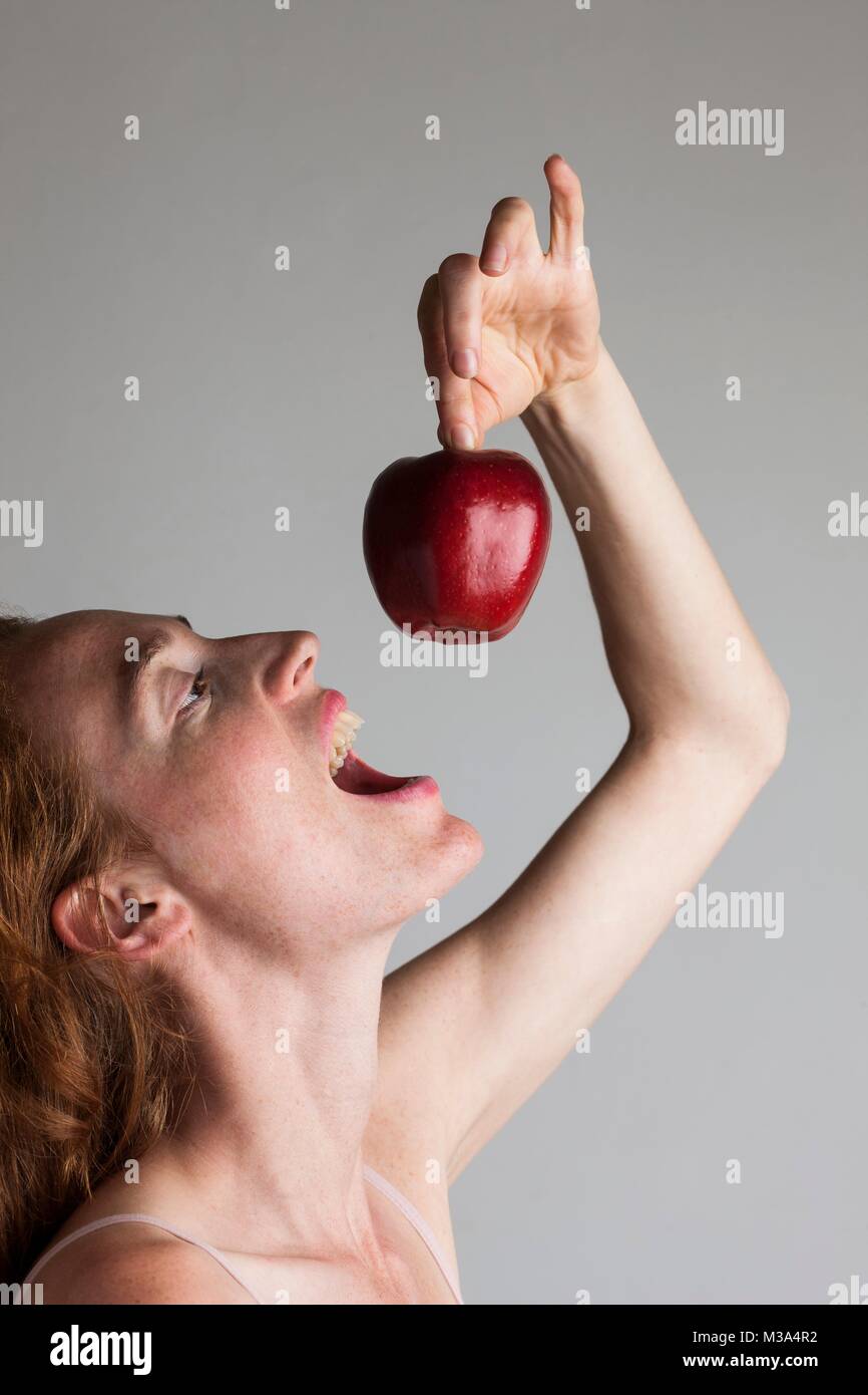 Parution du modèle. Profile of woman holding Red Apple au-dessus de sa tête avec la bouche ouverte. Banque D'Images