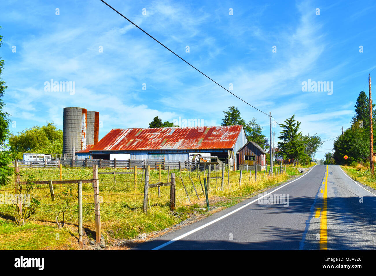Un chemin rural avec une ferme d'un côté et des poteaux de téléphone de deux côtés. Un fil barbelé est aux côtés de la route, la protection des terres agricoles. Une yello Banque D'Images