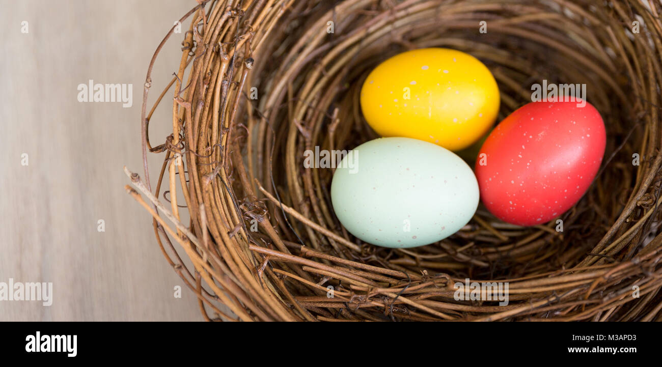 Close up of les oeufs de Pâques colorés dans un nid rustique ou un panier sur fond de bois. Mise à plat, vue du dessus, high angle avec copie espace. La lumière naturelle. Banque D'Images