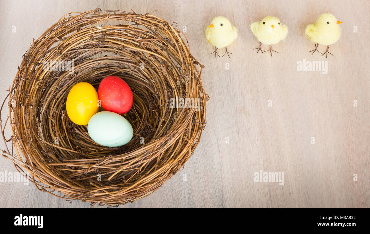 Les oeufs de Pâques colorés lumineux avec des poussins en nid rustique ou un panier sur fond de bois. Mise à plat avec l'exemplaire de l'espace. La lumière naturelle. Focus sélectif. Banque D'Images