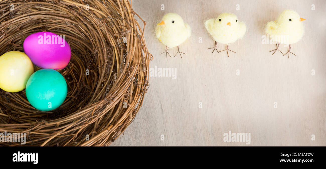Les oeufs de Pâques colorés lumineux avec des poussins en nid rustique ou un panier sur fond de bois. Mise à plat avec l'exemplaire de l'espace. La lumière naturelle. Focus sélectif. Banque D'Images