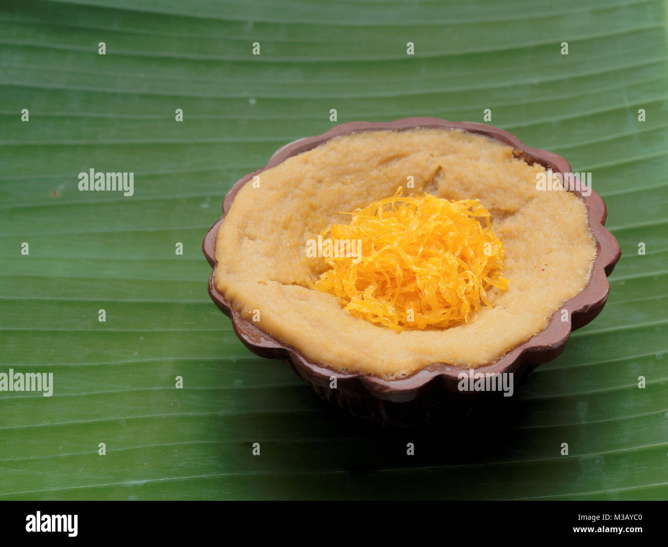 Dessert thaï, crème d'oeufs avec le riz gluant sucré surmonté de fils d'or, sur fond de feuilles de banane Banque D'Images