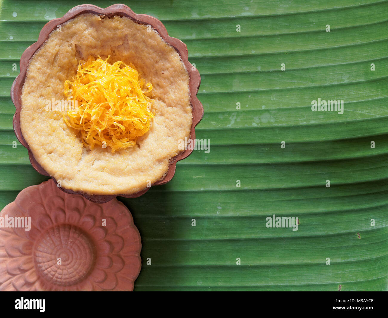 Dessert thaï, crème d'oeufs avec le riz gluant sucré surmonté de fils d'or, sur fond de feuilles de banane Banque D'Images