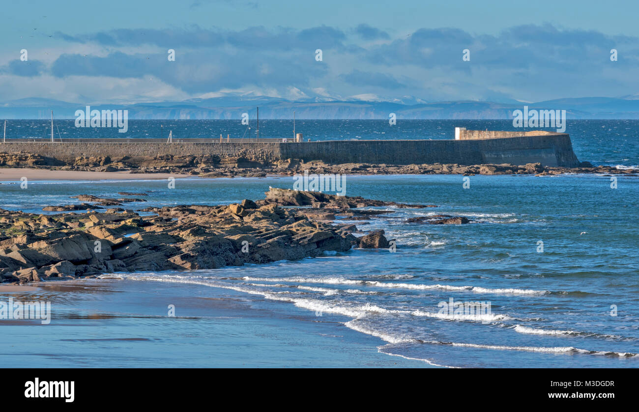 HOPEMAN SCOTLAND MORAY LE MUR DU PORT ET DE LA PLAGE AVEC LE BLACK ISLE ET MONTAGNES COUVERTES DE NEIGE DANS LA DISTANCE Banque D'Images