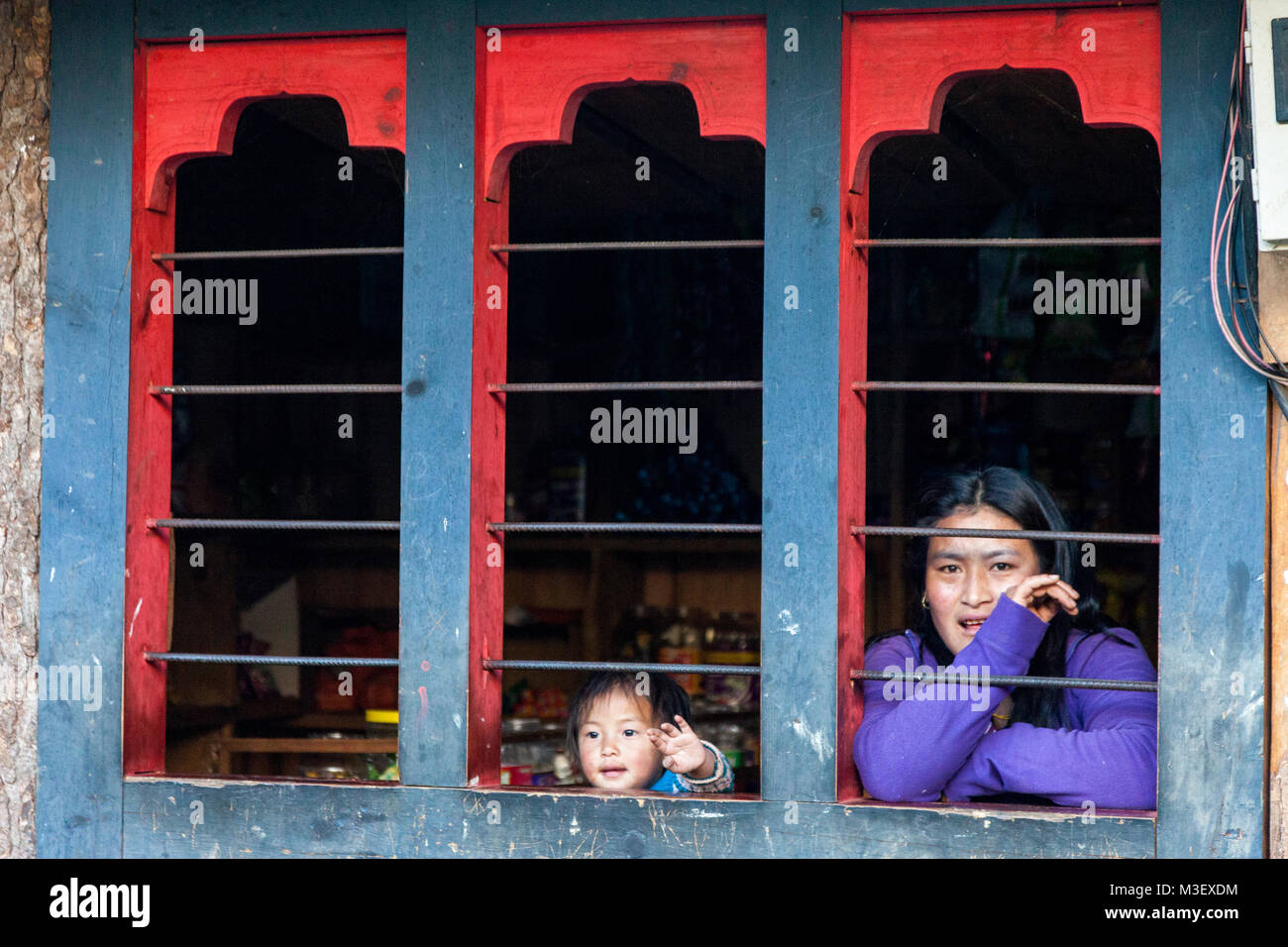 Le Bhoutan, Phobjikha. Femme et petite fille à la fenêtre de boutique, Kikorthang Village. Banque D'Images