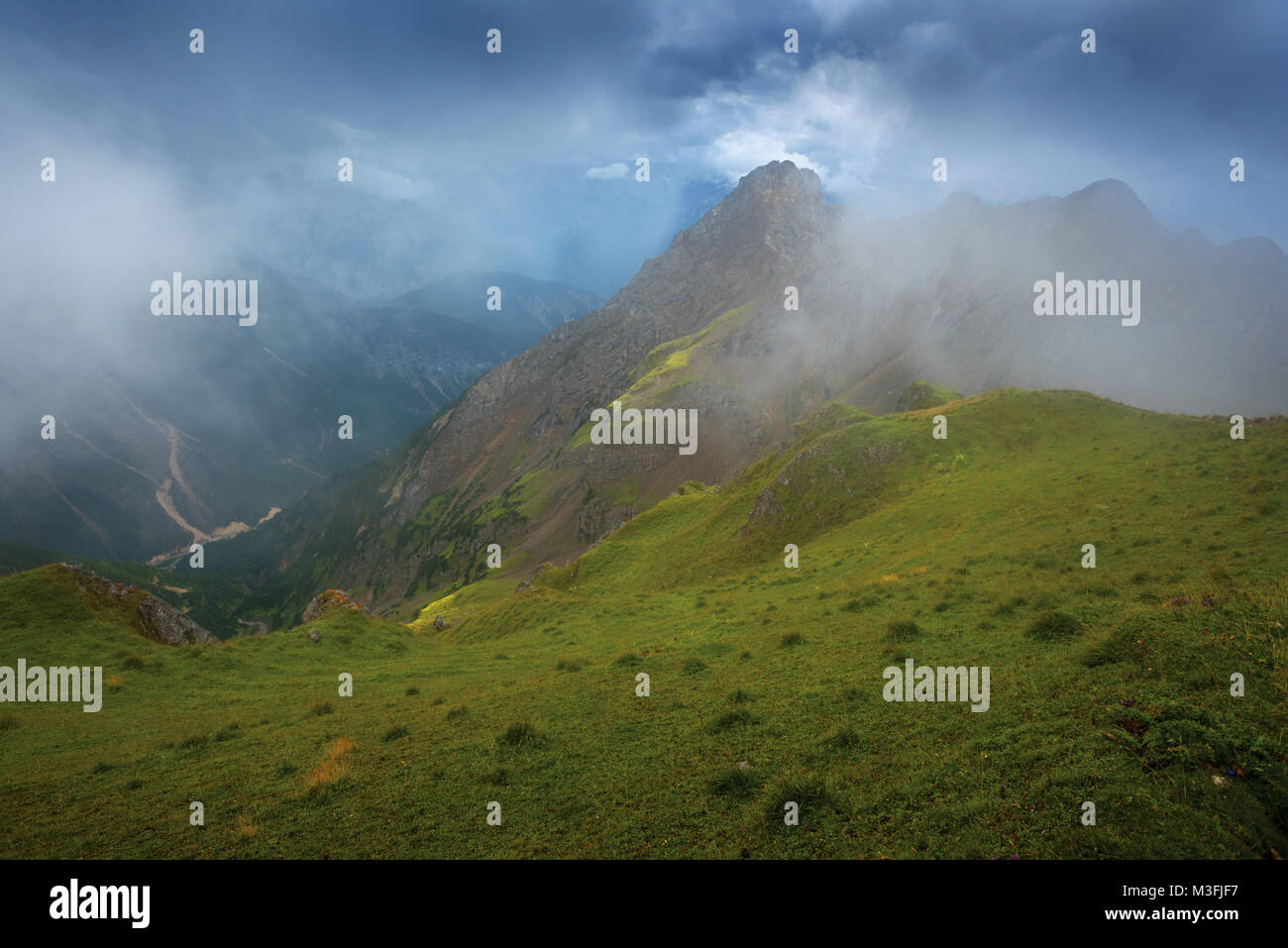 En ordre décroissant pente gazonnée, sommets de montagne sous des nuages orageux Banque D'Images