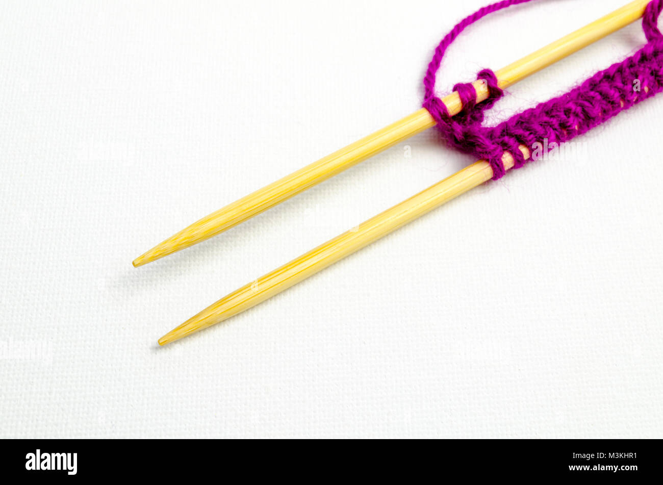 Un studio photo d'une paire d'aiguilles à tricoter en bois avec tricot violet Banque D'Images