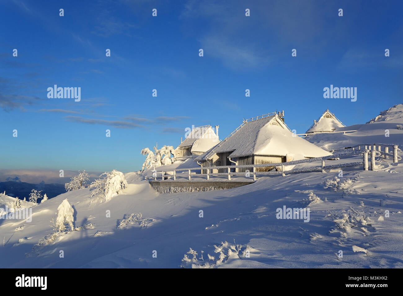 Vieux bois gelés idyllique alpine cabines couvertes de neige dans le paysage de montagne de Velika planina, la Slovénie au coucher du soleil. Banque D'Images