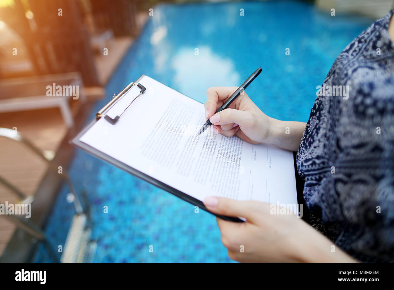 Close-up de main de jeune femme signature document sur fond de journée ensoleillée piscine. Utilisé avant avec Open Font License Banque D'Images