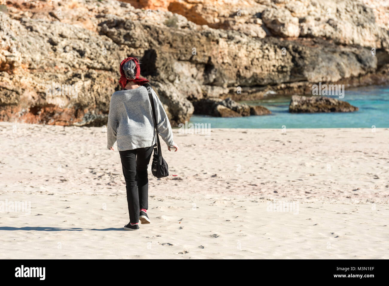 Une jeune femme brune aux cheveux gris se promène avec un foulard rouge sur la tête du Cala Romantica à Palma de Mallorca, Espagne. Banque D'Images