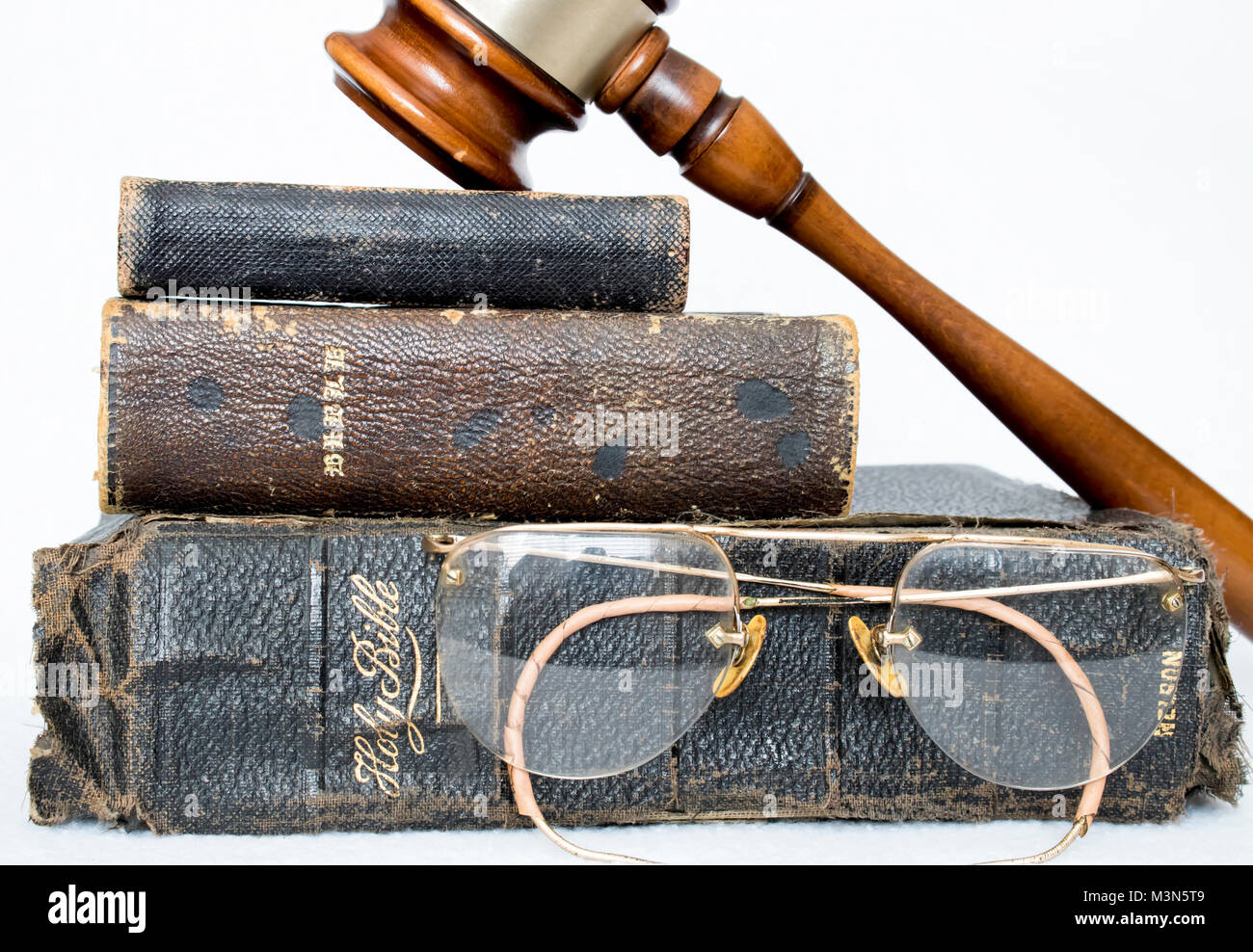 Près pile de bibles ancien en cuir avec marteau et meubles anciens verres sur fond blanc Banque D'Images