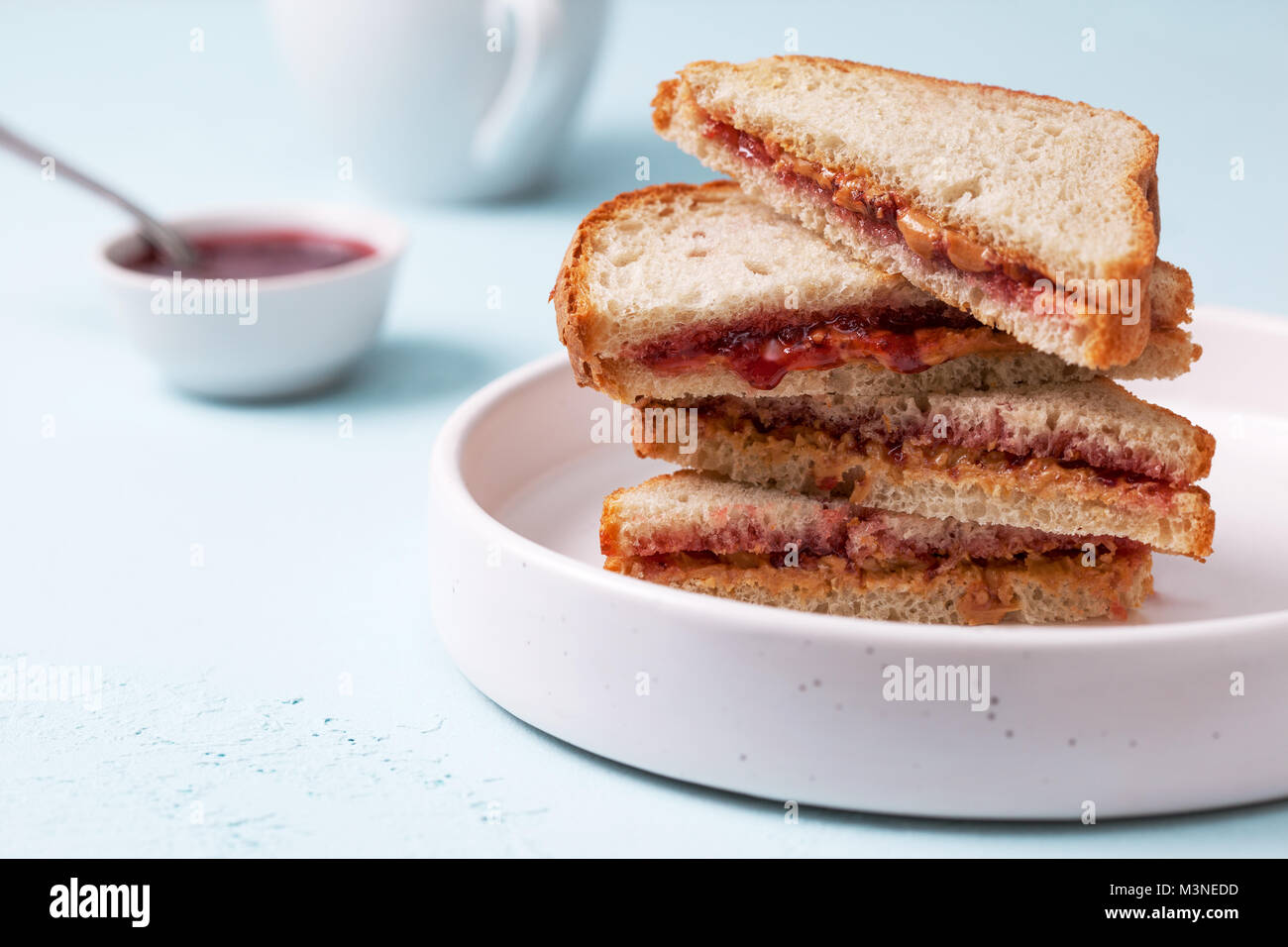 Toast avec du beurre d'arachide et de la confiture dans un plat en céramique blanche sur un fond de béton bleu Banque D'Images