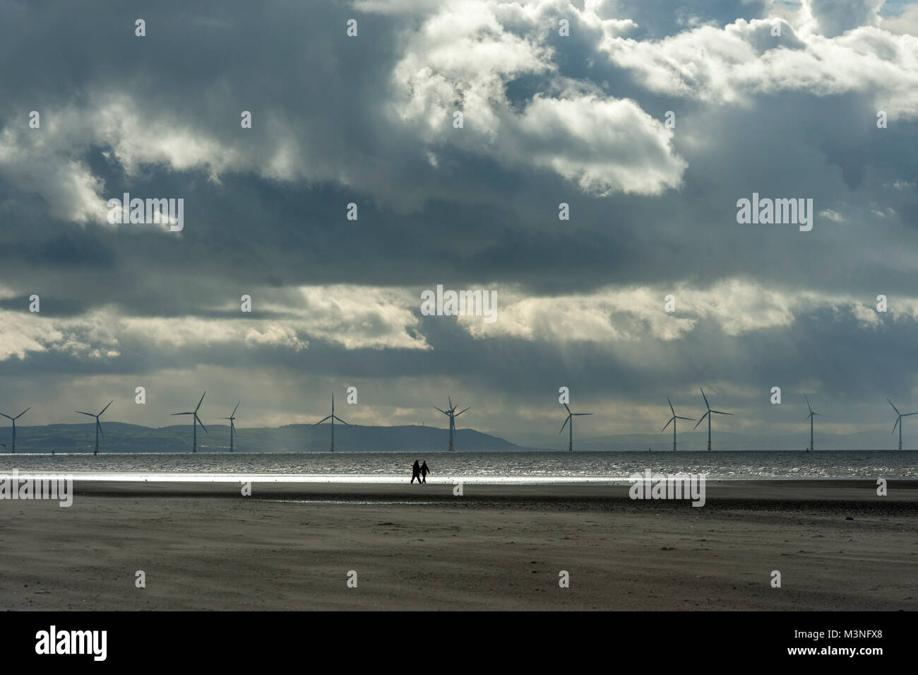 Une promenade le long de la plage près de Crosby avec Burbo Bank éoliennes en mer dans le Merseyside Sefton distance comme le soleil se reflète sur la mer en Liv Banque D'Images