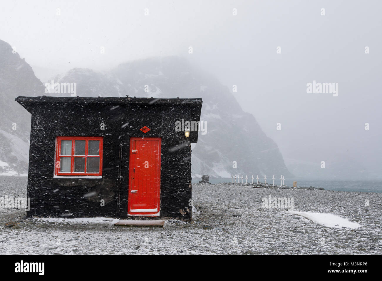 Soufflage horizontal vent tempête de neige ancienne cabane de chasse à l'avant-plan, vieux cimetière des baleiniers et les montagnes côtières en dehors de l'Antarctique fond blanc neige Banque D'Images