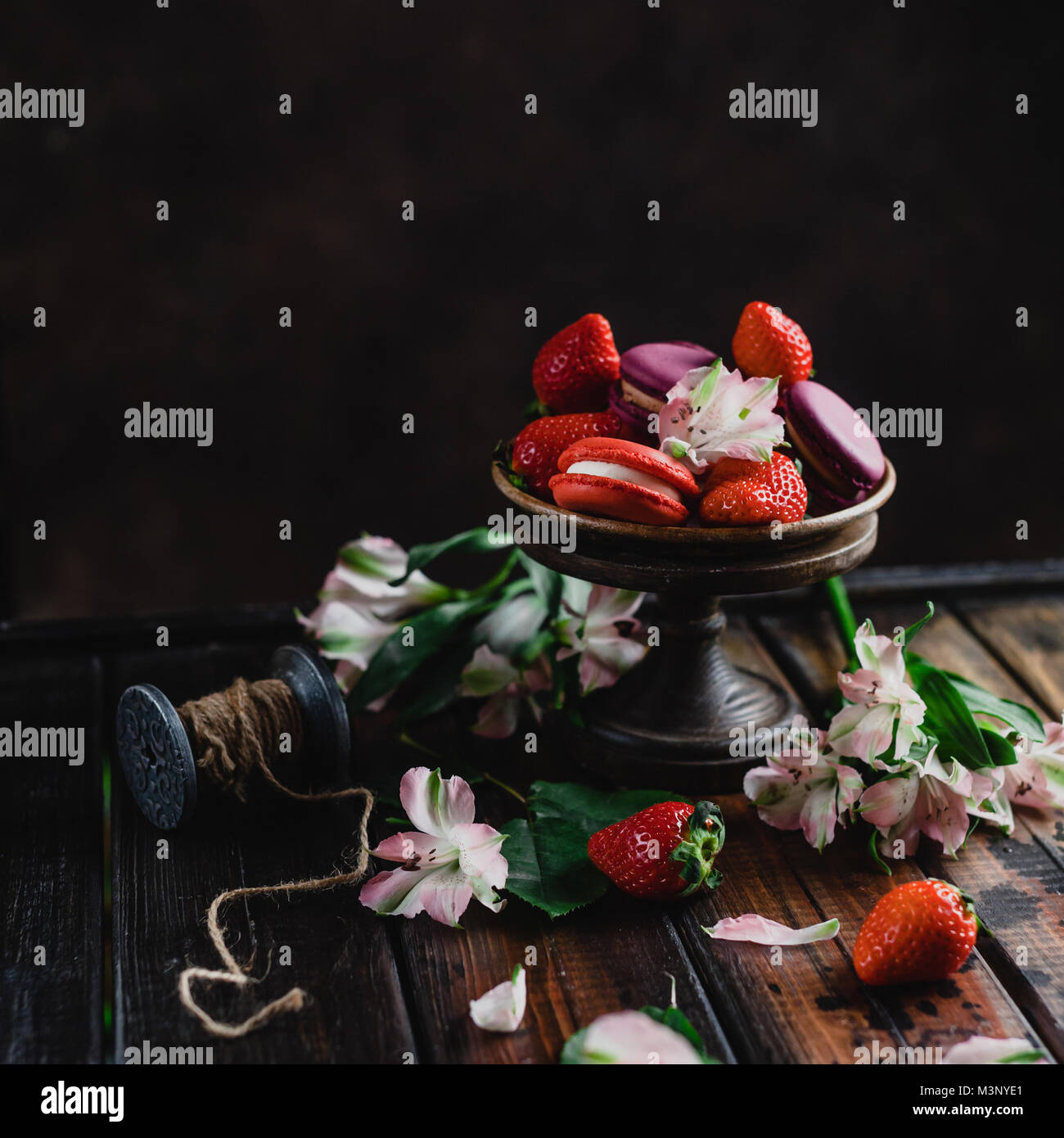 Bol de bonbons macarons et fraises sur table en bois avec des fleurs Banque D'Images