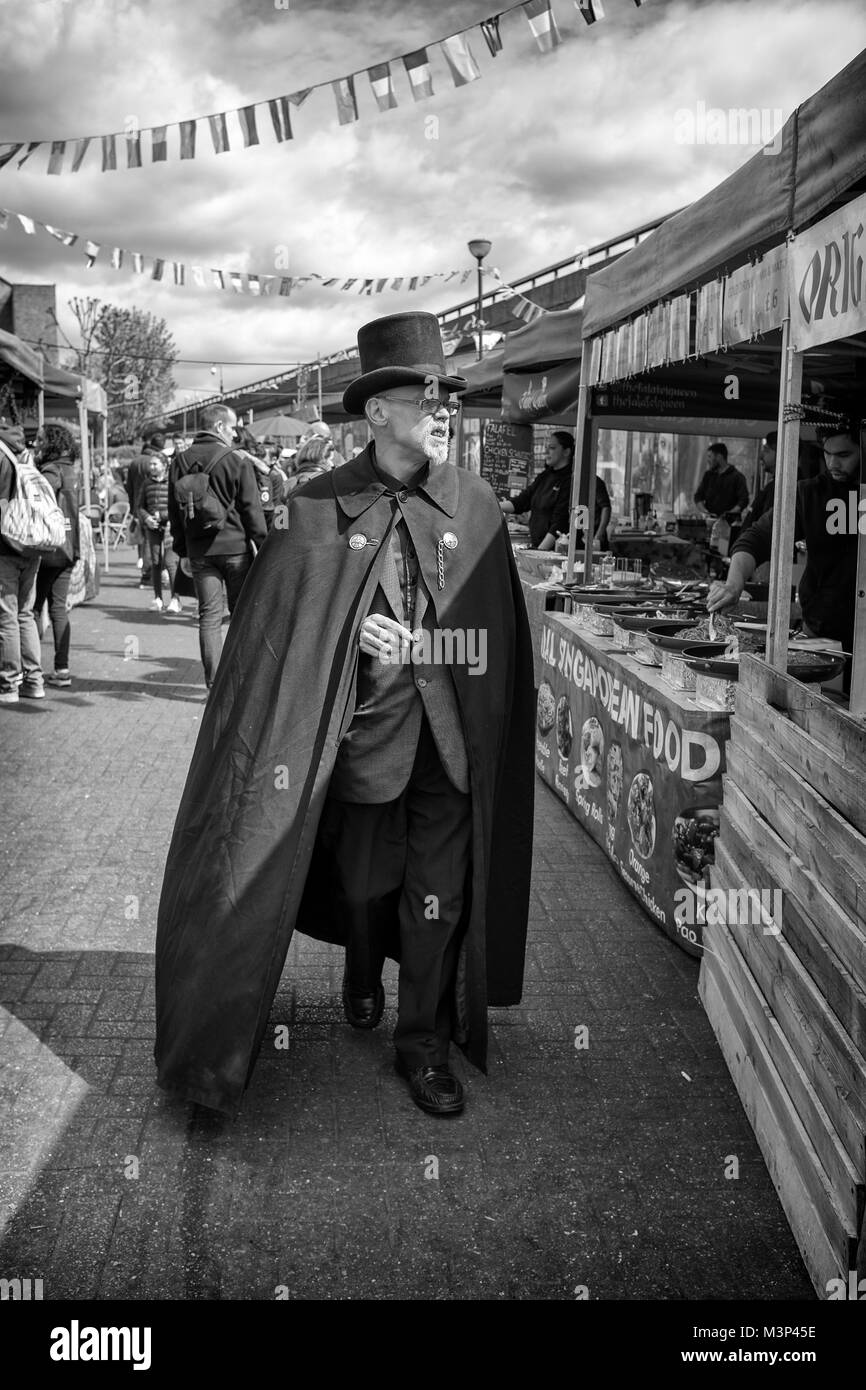 Photographie noir et blanc d'un excentrique de l'homme en haut de forme et cape marcher le long de Portobello Road, Notting Hill, à l'ouest de Londres, Angleterre, Royaume-Uni, Banque D'Images