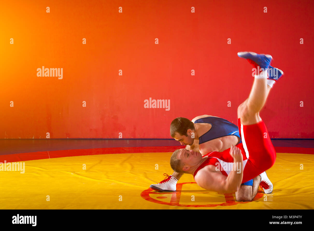 Deux lutteurs forte en bleu et rouge wrestling collants sont wrestlng et prendre une décision d'un jet de la hanche sur un tapis de lutte jaune dans la salle de sport. Les jeunes ma Banque D'Images