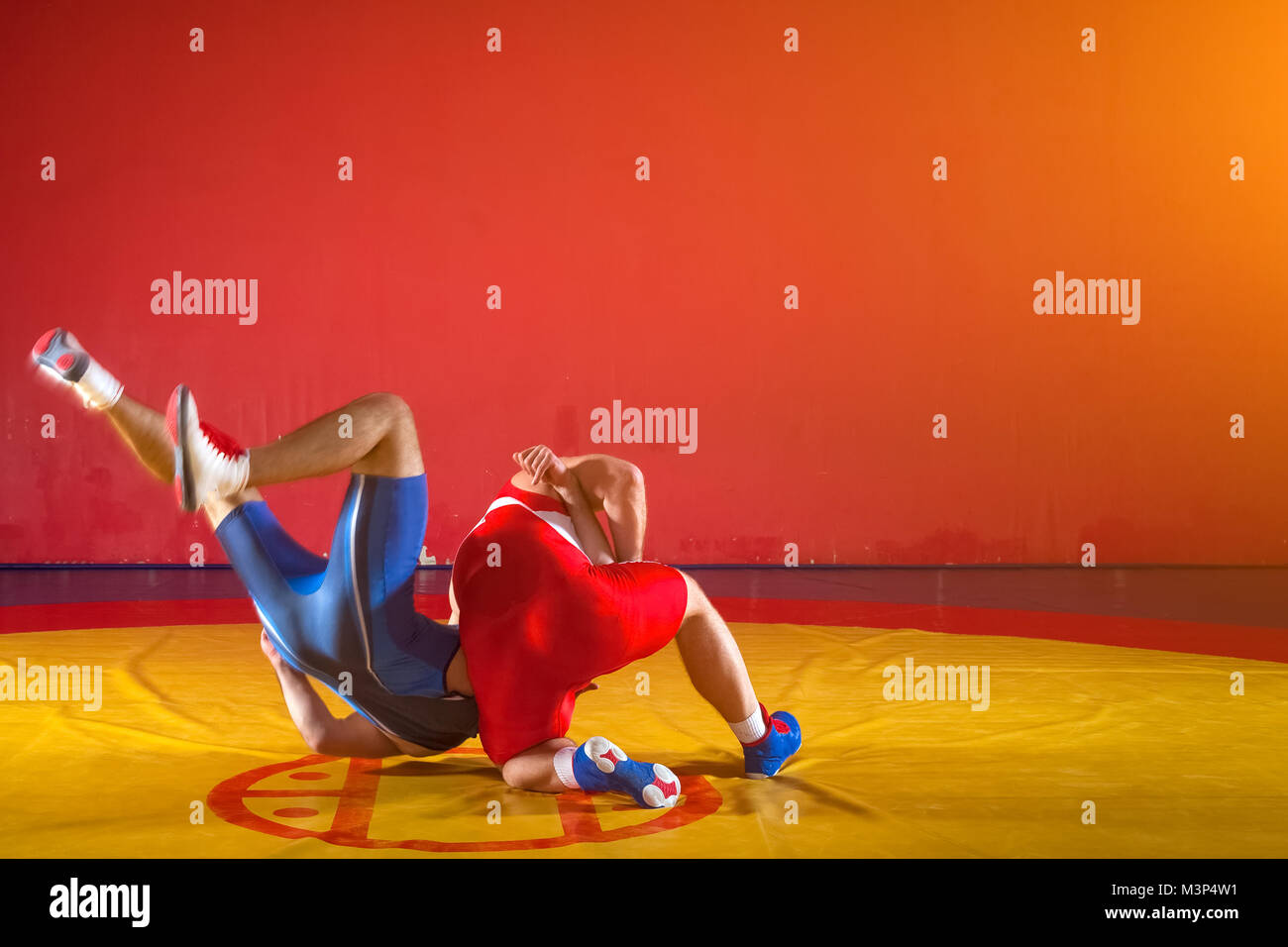 Deux lutteurs forte en bleu et rouge wrestling collants sont wrestlng et faire une suplex wrestling wrestling jaune sur un tapis dans la salle de sport. Jeune homme ne Banque D'Images