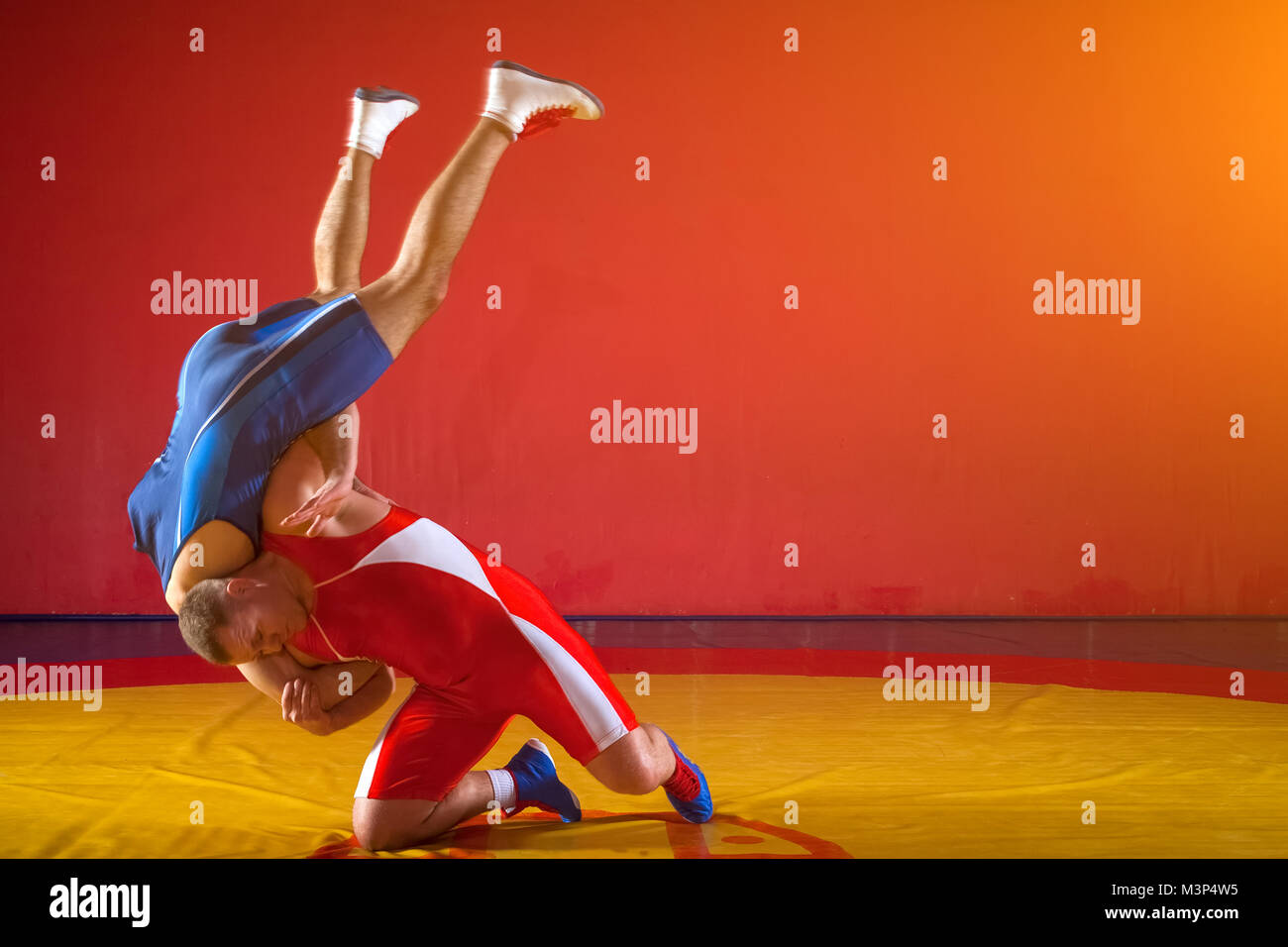 Deux lutteurs forte en bleu et rouge wrestling tights faisant un jet de hanche sur un tapis de lutte jaune dans la salle de sport. Jeune homme faisant face. Banque D'Images