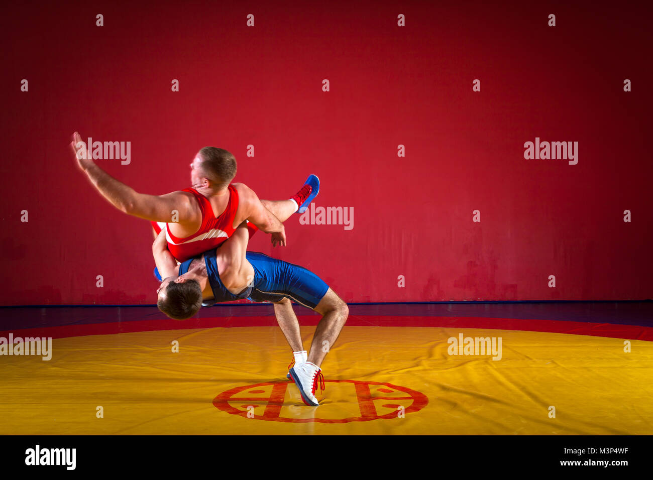 Deux lutteurs gréco-romain en uniforme rouge et bleu faire une suplex wrestling wrestling jaune sur un tapis dans la salle de sport Banque D'Images