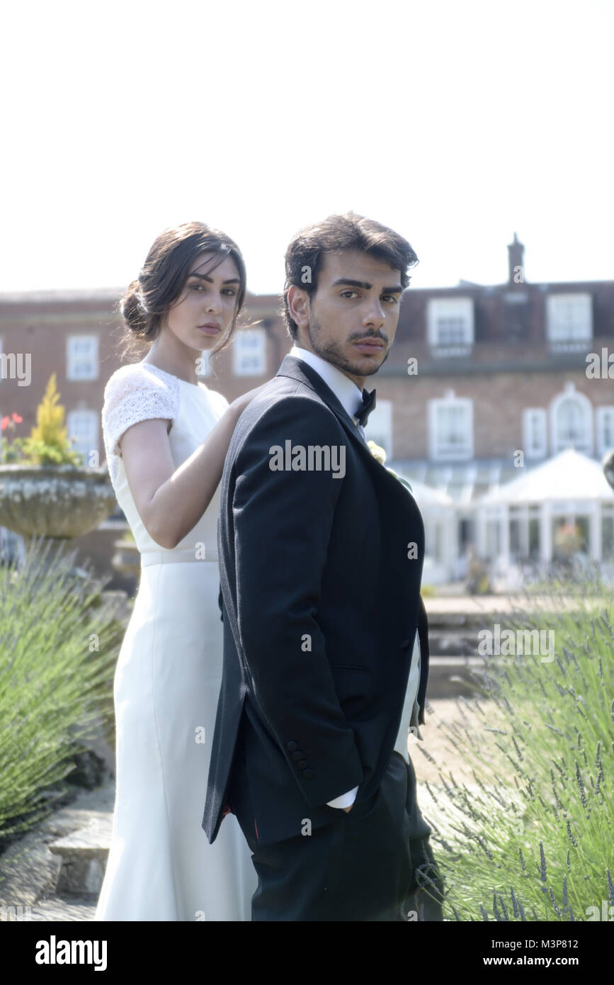 Un beau couple aux cheveux noirs le jour de leur mariage posent ensemble en face d'un manoir anglais, par une belle journée ensoleillée Banque D'Images