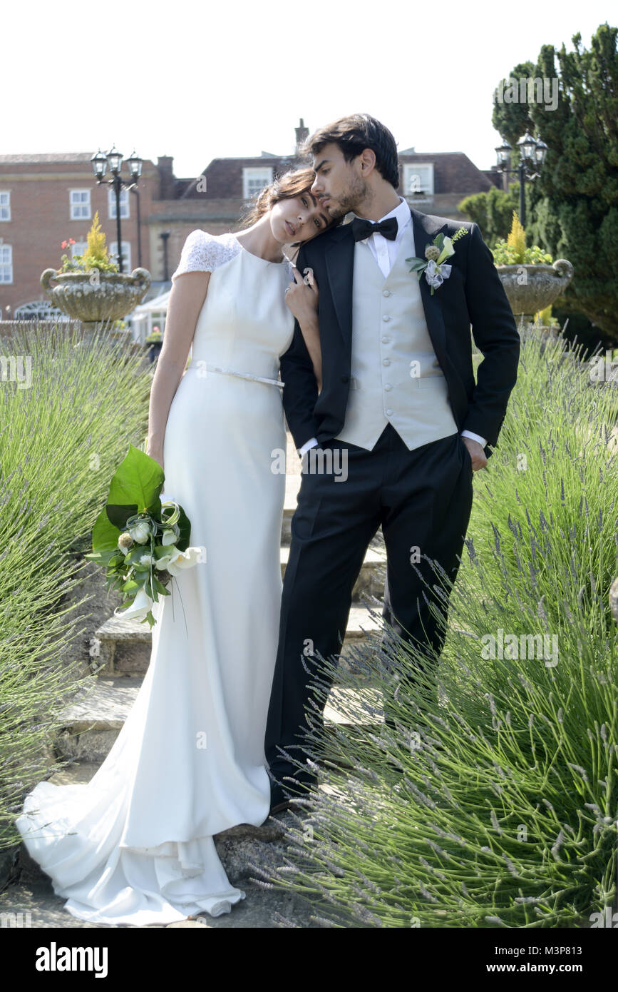 Un beau couple aux cheveux noirs le jour de leur mariage posent ensemble en face d'un manoir anglais, par une belle journée ensoleillée Banque D'Images