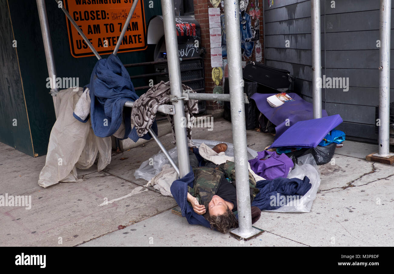 Sans-abri endormi sur le trottoir dans la rue de Manhattan après avoir fait une maison dans le cadre de la construction d'échafaudage des poteaux. Banque D'Images