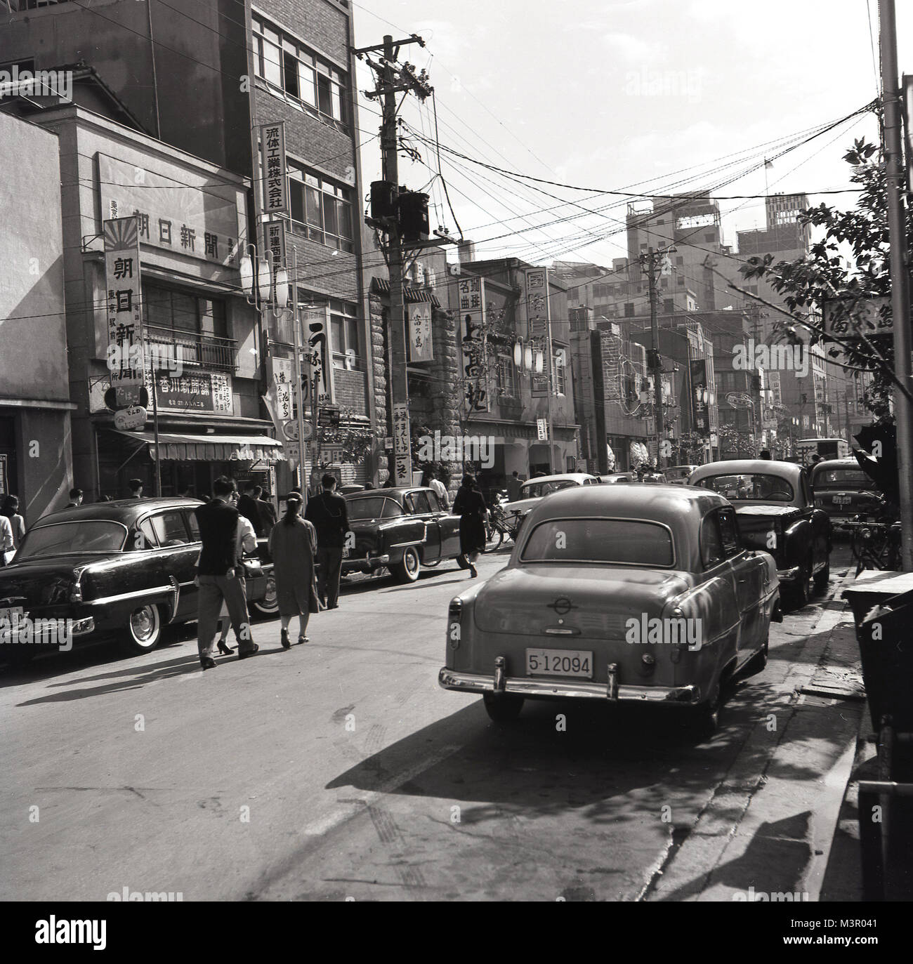 Années 1950, tableau historique d'une rue de la vieille ville de Tokyo, au Japon, avec de nombreuses grandes voitures de style américain de l'époque stationné sur le côté de la route. Banque D'Images