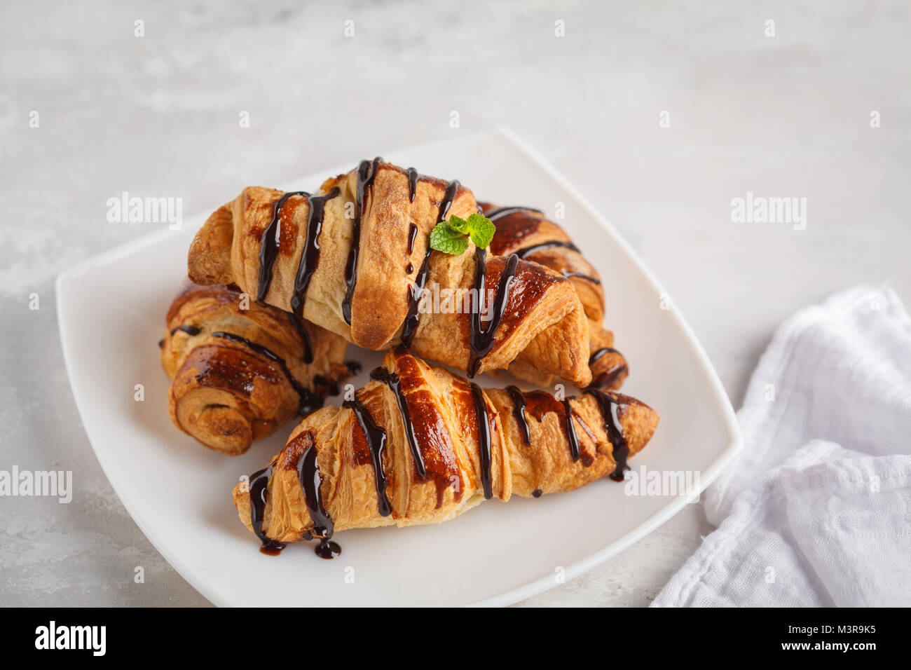 Des croissants frais avec du sirop de chocolat sur un fond gris clair, copiez l'espace. La cuisine française dessert concept. Banque D'Images