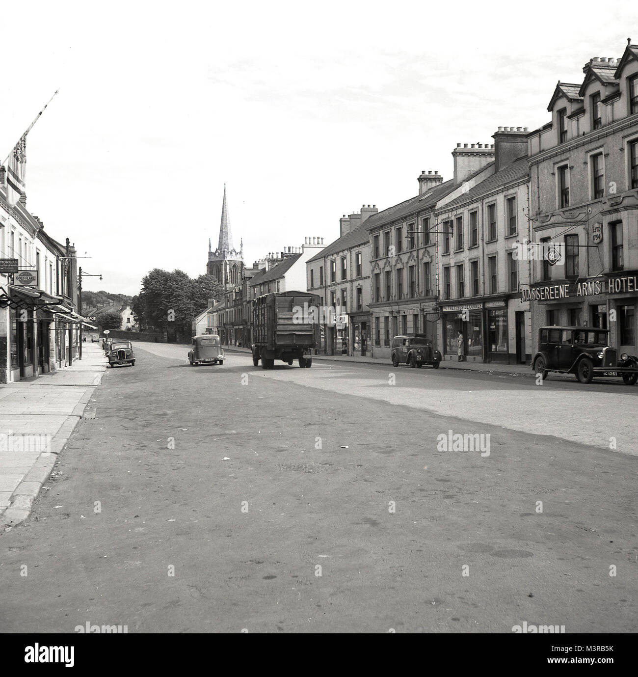 Années 1950, tableau historique d'Antrim High Street, l'Irlande du Nord, montrant les bâtiments, magasins, l'Massereene Arms Hotel et les véhicules de cette époque. L'hôtel, vu sur la droite, a été construit en 1754. Banque D'Images