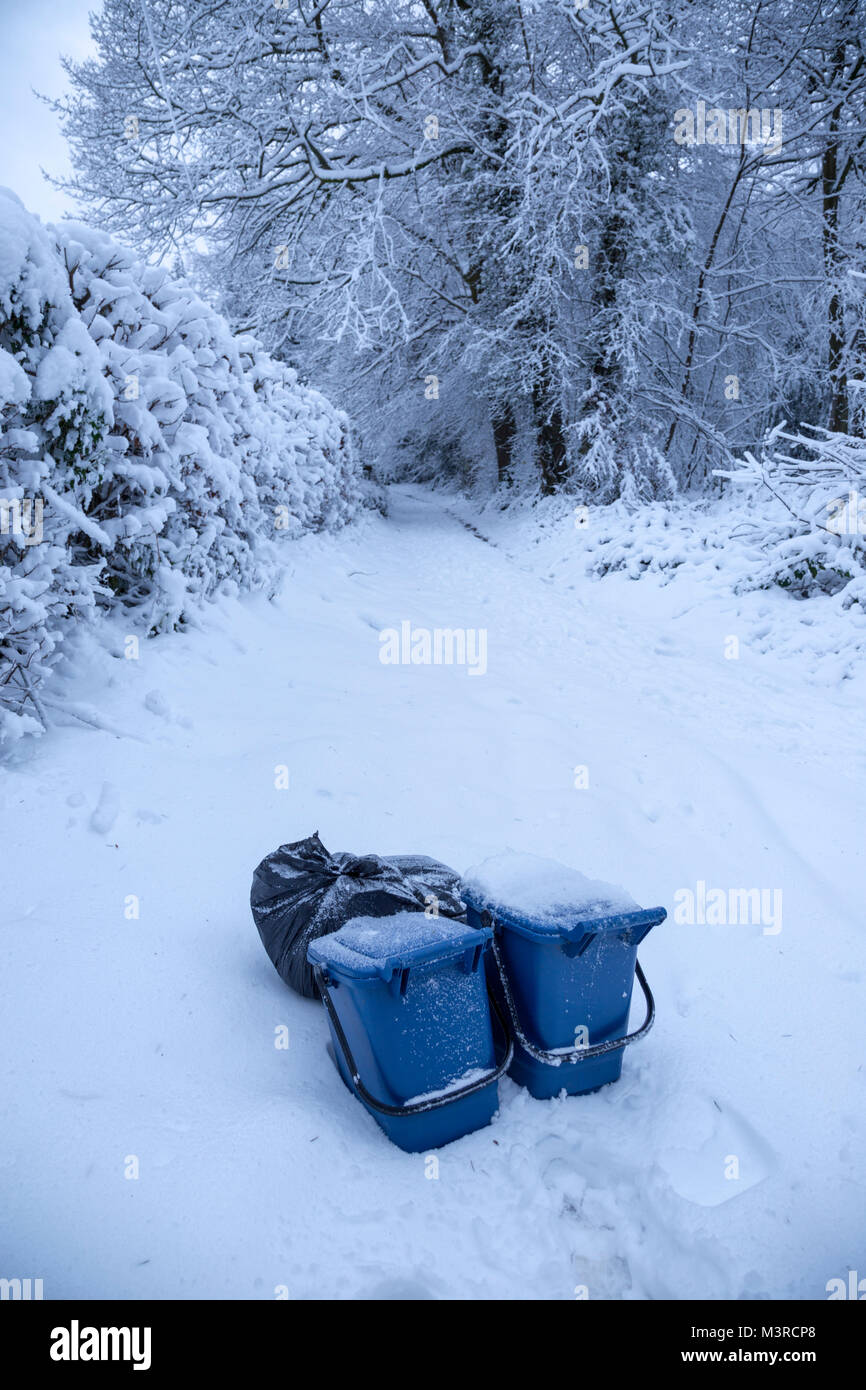 Des poubelles en plastique bleu collection en attente sur une étroite route de campagne Monmouthshire après la nuit de neige. Banque D'Images