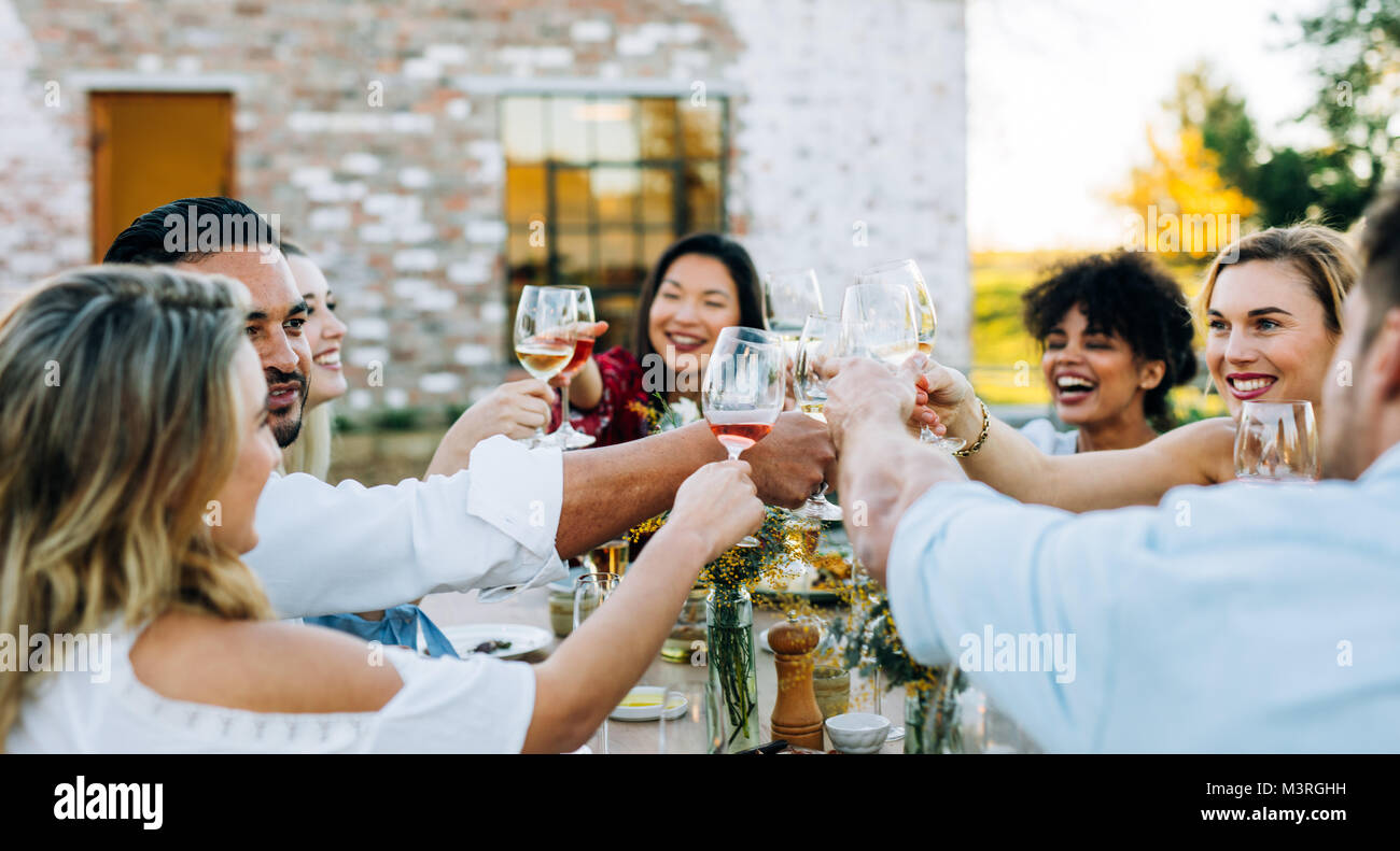 Groupe d'hommes et de femmes toasting wine at outdoor party. Les personnes ayant des boissons pendant le déjeuner au restaurant le jardin. Banque D'Images