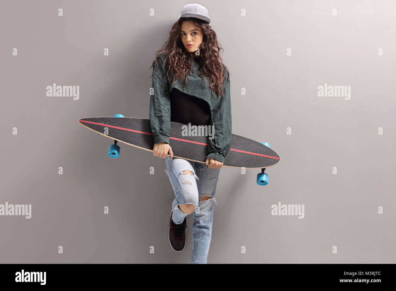 Adolescente avec un longboard appuyé contre un mur gris Banque D'Images