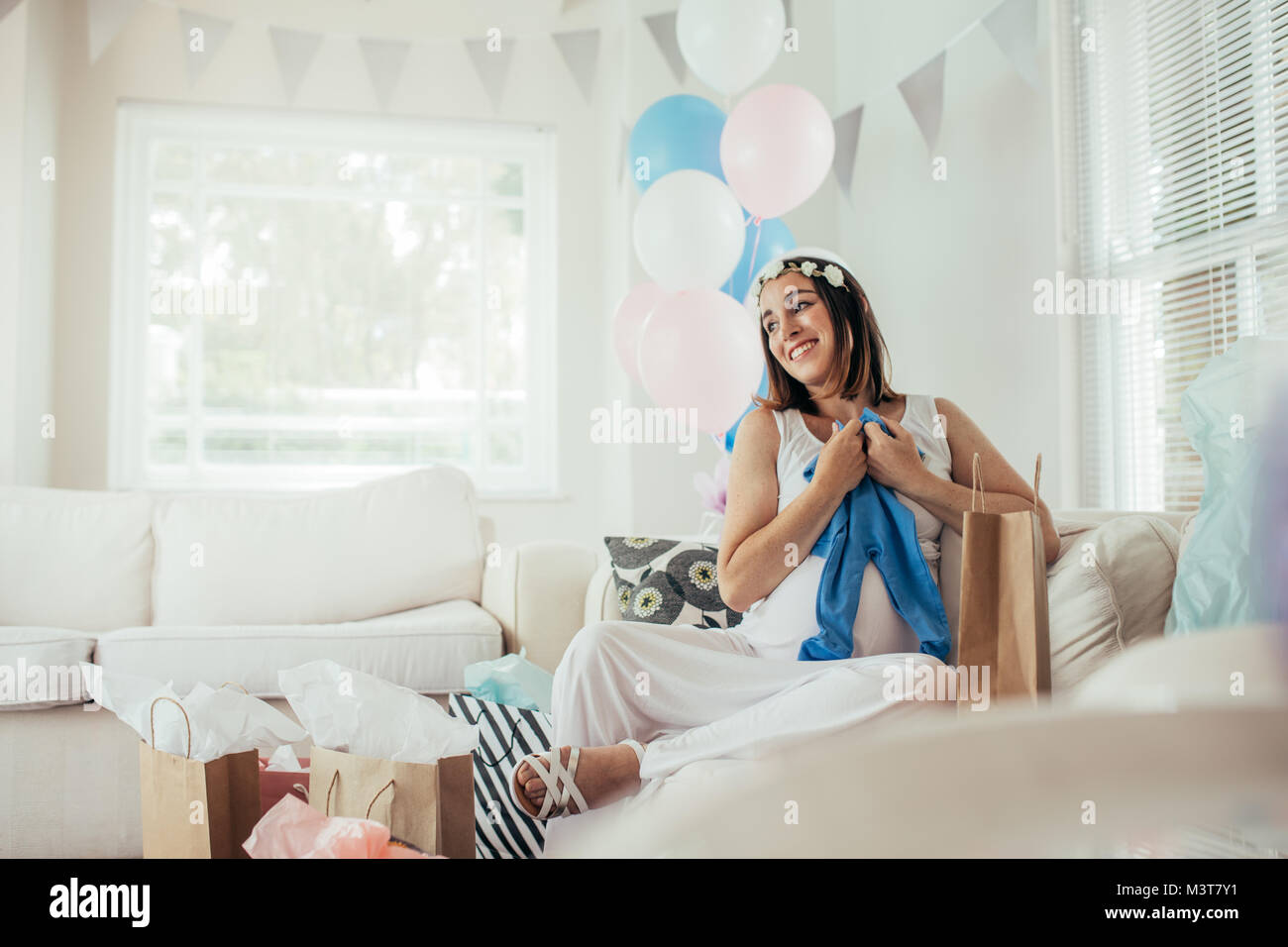 Smiling young pregnant woman sitting on sofa avec de nouveaux cadeaux à partie de douche de bébé. S'attendant à la mère à la layette et souriant. Banque D'Images
