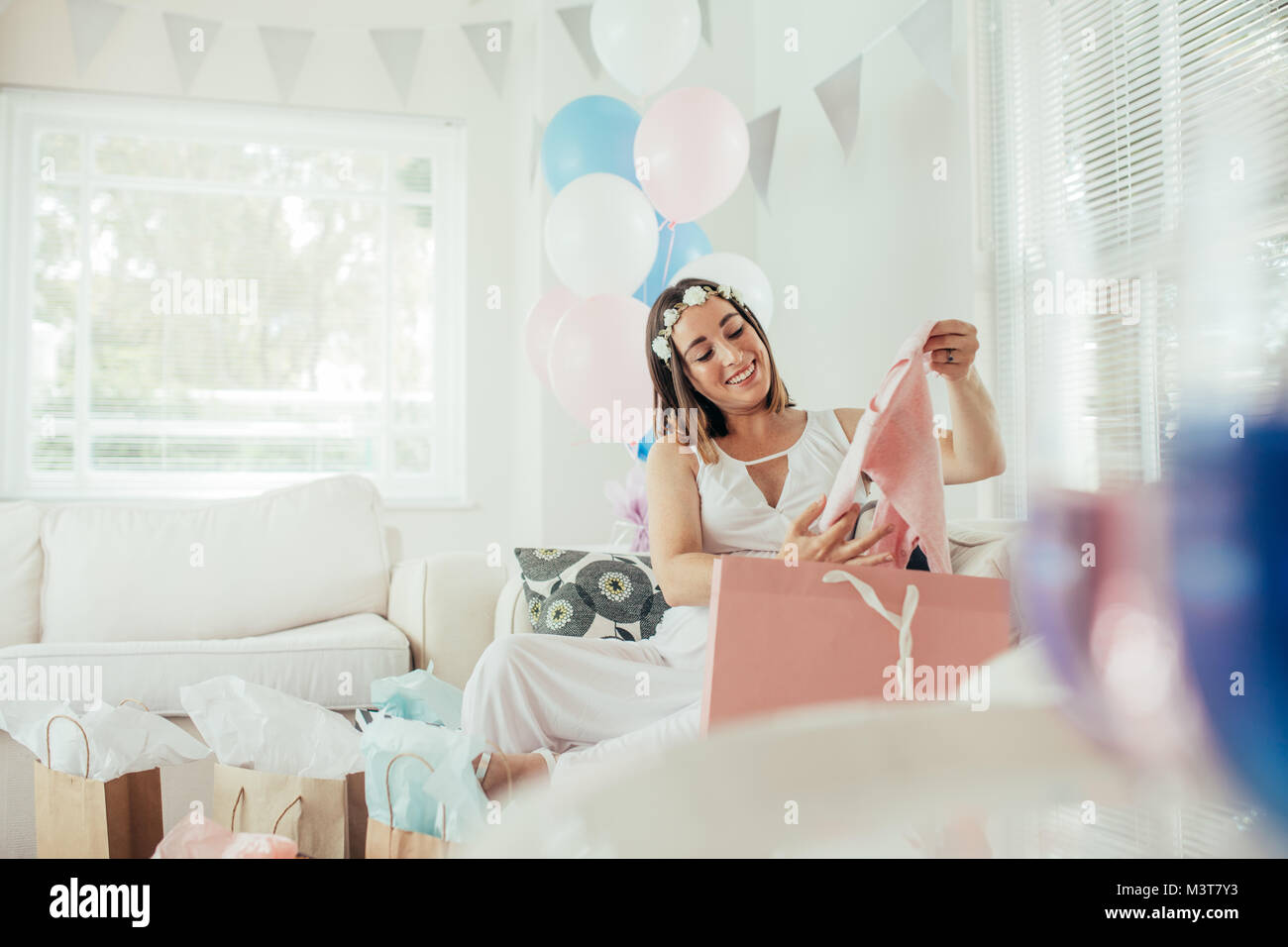 Mère prévoyante sort de nouveaux vêtements pour bébé douche. Ouverture féminine présente reçu lors de partie de douche de bébé. Banque D'Images