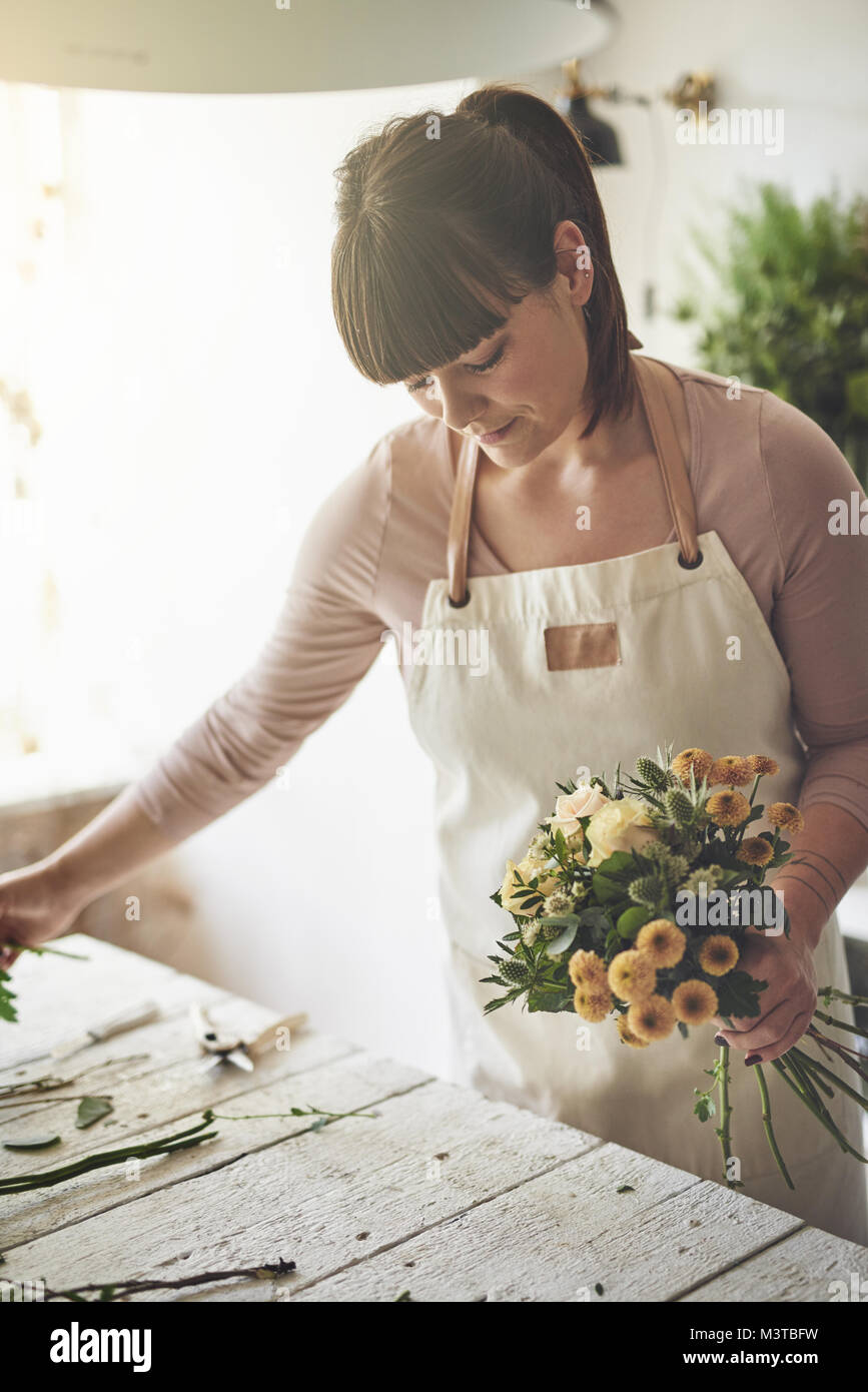 Smiling young female florist standing at a table dans sa boutique de fleurs un bouquet de fleurs Banque D'Images
