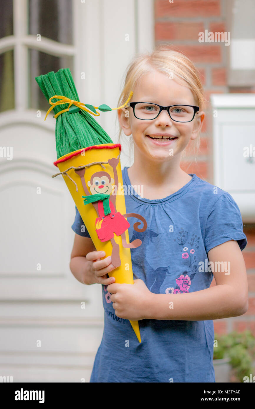 Une fille blonde à lunettes se réjouit de sa première journée à l'école et pose avec le sac d'école sur sa porte. Banque D'Images