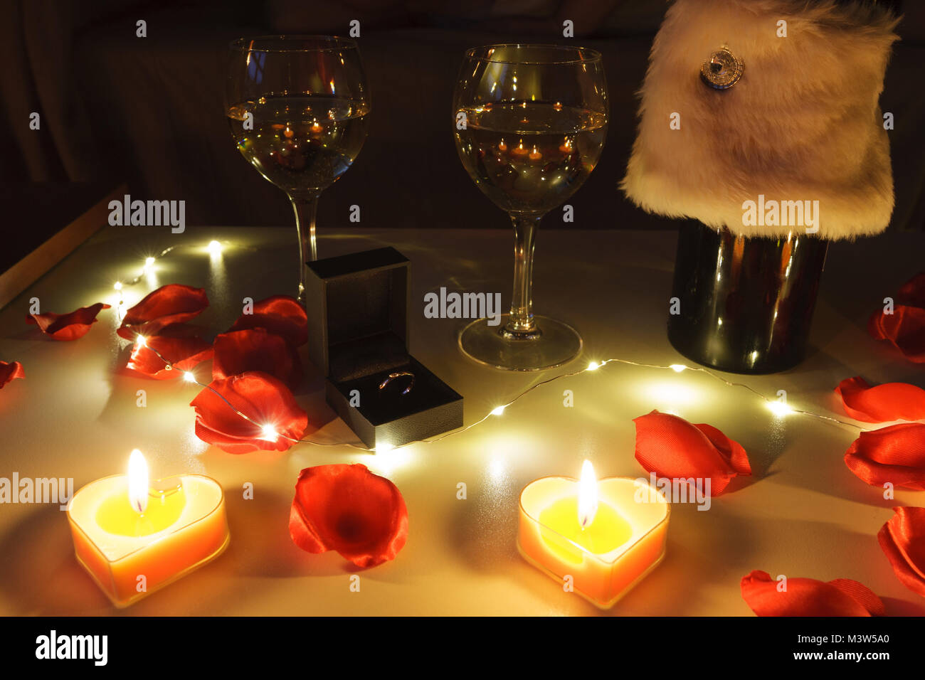 Vue rapprochée d'un dîner romantique table avec verres de vin, des roses, des bougies et une bague de fiançailles Banque D'Images