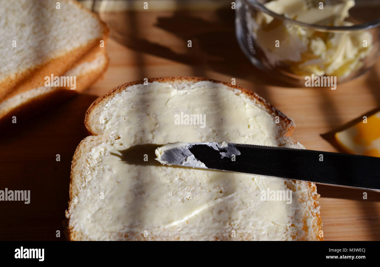 Le pain blanc avec Mayo sur elle montré face ouverte avec l'ensemble de couteaux en argent de style. Le beurre dans un plat en verre et le pain blanc a également indiqué. Les ombres. Banque D'Images