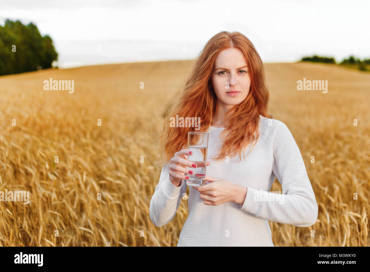 Les jeunes red-haired woman standing in the wild et tenant un verre d'eau potable. Banque D'Images