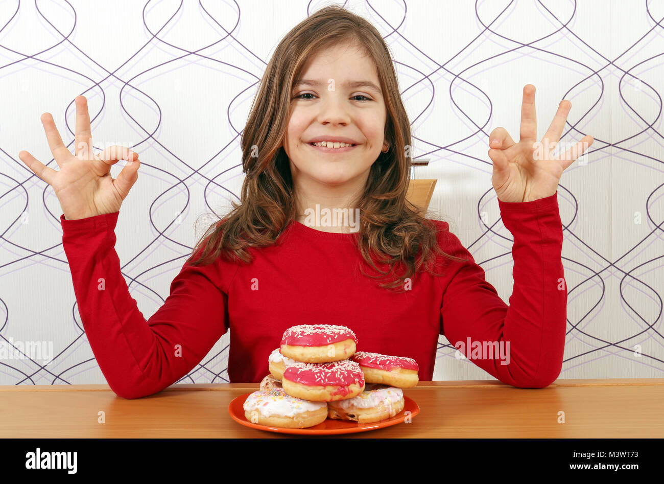 Happy little girl avec des beignets sucrés et signes des mains ok Banque D'Images