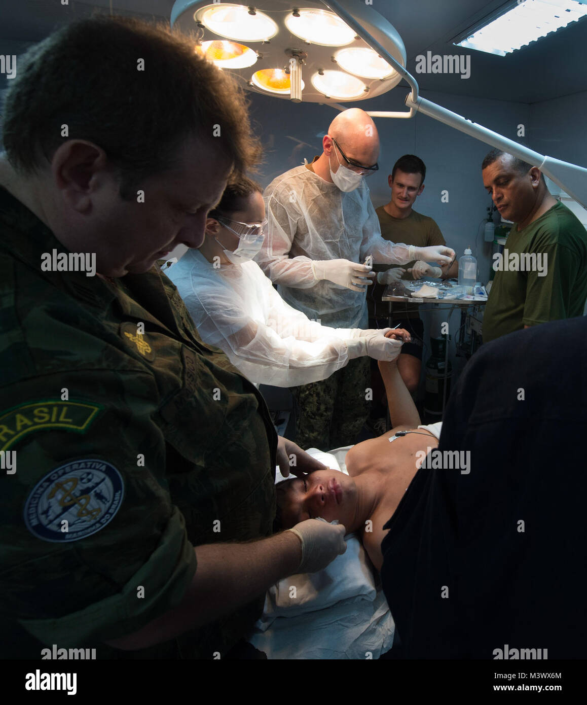 171127-N-QM691-0580 fleuve Amazone, Brésil (nov. 27, 2017) Le Cmdr. Carlos Marco, Manaus, Directeur de la polyclinique de la Marine à gauche, le confort d'un 14-year-old boy indigènes à bord NAsH Soares de Meirelles, sur l'Amazone au Brésil. Le lieutenant Cmdr. Thomas Barlow, un médecin de la Marine américaine, la droite, et le 1er lieutenant Priscila Tomy Ribeiro, un médecin brésilien, milieu, nettoyer la blessure par balle dans la main du garçon. Après la blessure, la famille du garçon avait salué l'ANSH Soares de Meirelles, qui passait le long de la rivière, et avait utilisé un petit bateau pour le conduire au navire pour l'attention médicale. Barlow est membre d'une équipe Banque D'Images