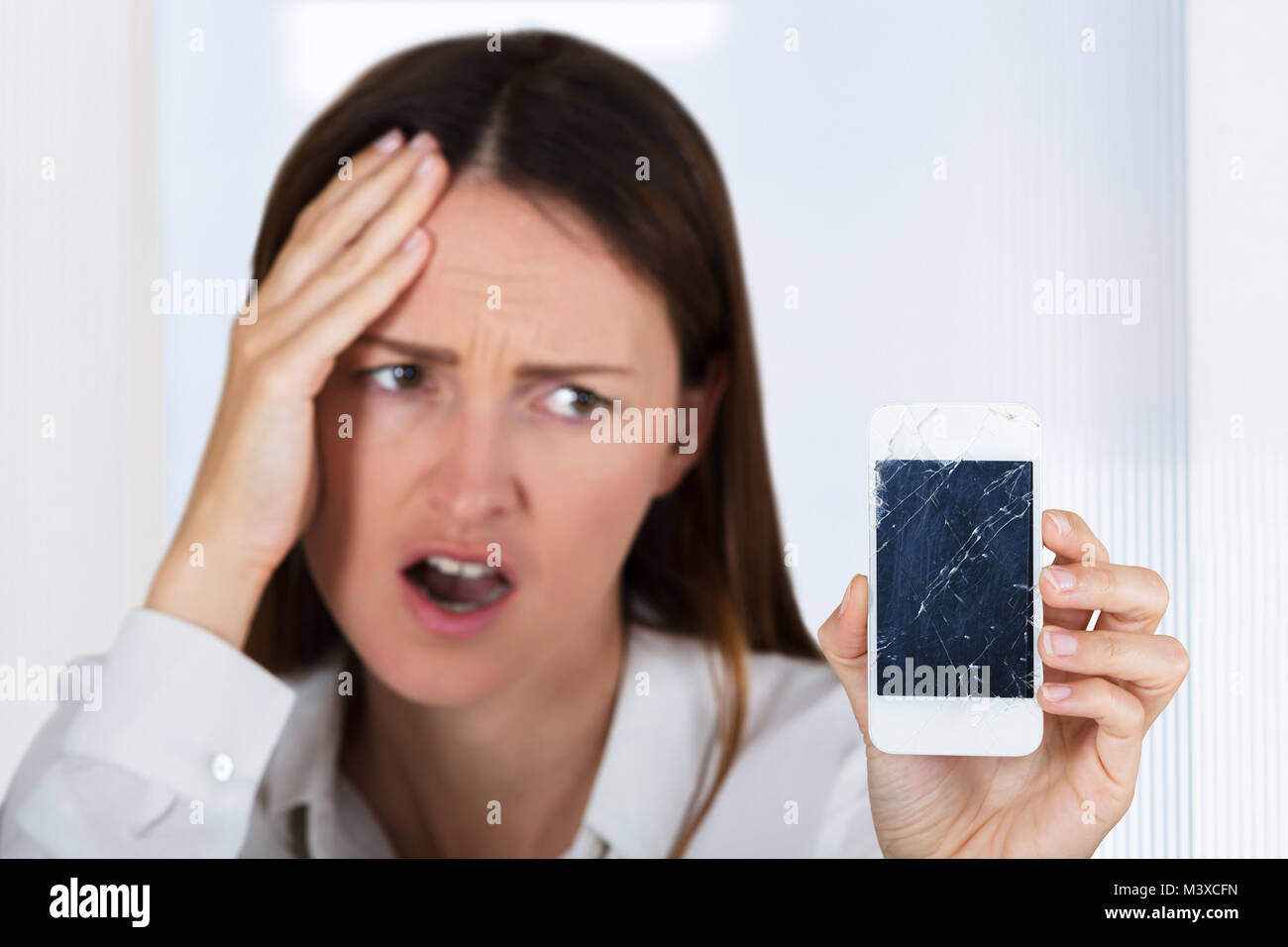 Close-up d'une jeune femme inquiète's Hand Holding Smartphone avec écran fissuré Banque D'Images