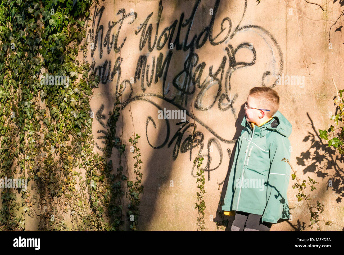 6 ans avec des lunettes debout à côté de la peinture en aérosol graffiti sur mur, qui lit ce que serait votre maman ?, Ecosse, Royaume-Uni Banque D'Images