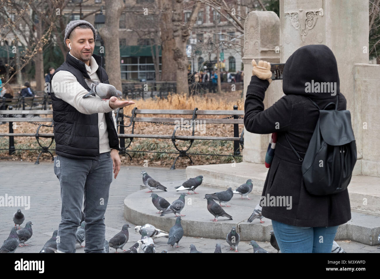 Un homme à Washington Square Park l'alimentation des pigeons et d'être photographié par sa compagne. Banque D'Images