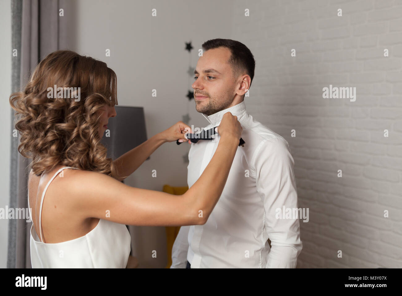 Bride fixe au nœud papillon sur groom s cou alors qu'ils sont habillés en chemise blanche Banque D'Images