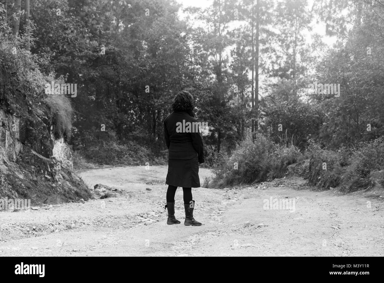 Jeune femme vêtue de noir dans une forêt brumeuse en noir et blanc Banque D'Images